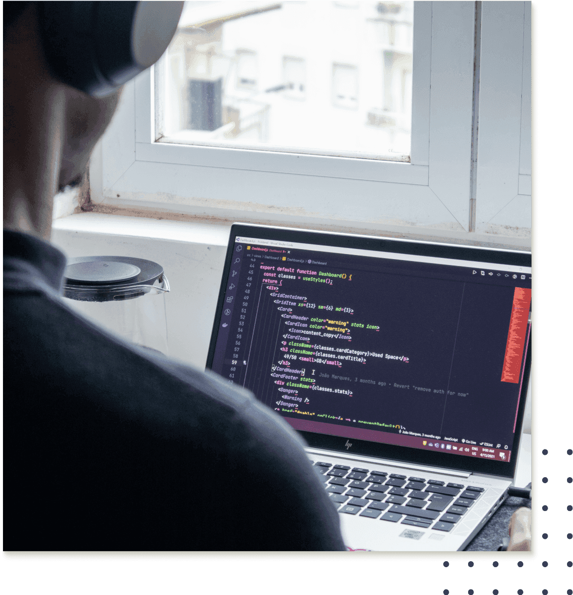 A man sitting at a laptop with headphones on and a window in the background