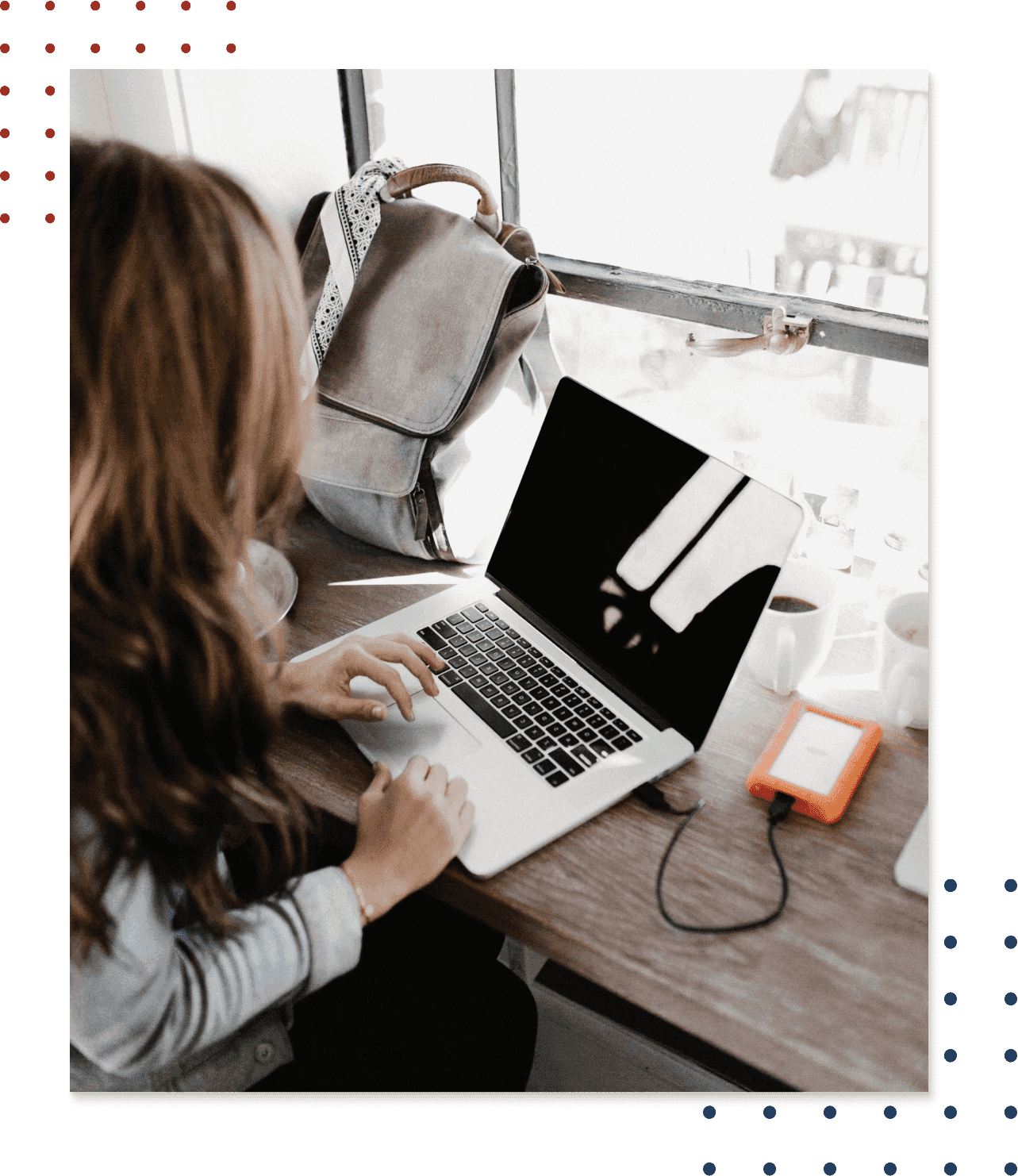 Woman sitting at a table with a laptop with a window in the background